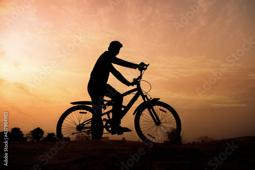 Silhouette of a man rides a bike at sunset. Orange sky background.