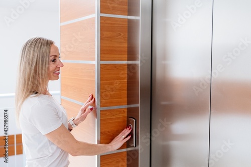 Smiling blonde woman calling elevator of the residential building.