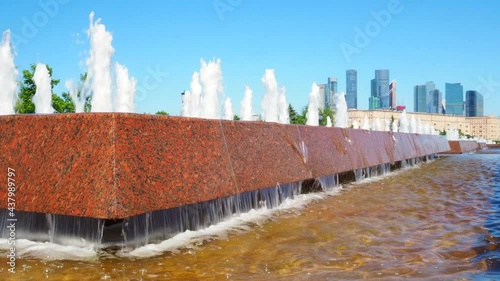 Jets of fountains on a sunny day against the backdrop of modern skyscrapers and a cloudless blue sky. Recreation area in Victory Park on Poklonnaya Hill in summer.