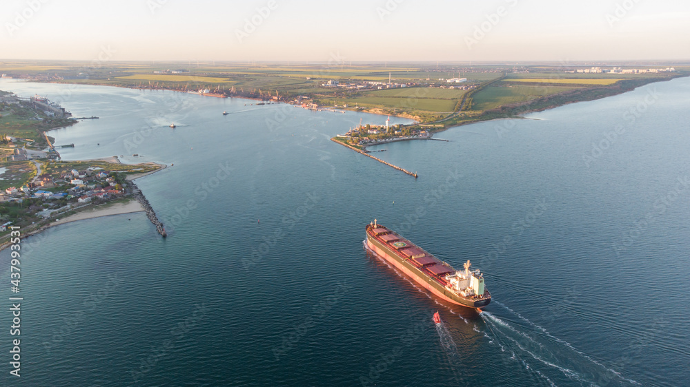 A large ocean-going cargo ship moves out to sea on calm waters. Dry cargo ship aerial view.