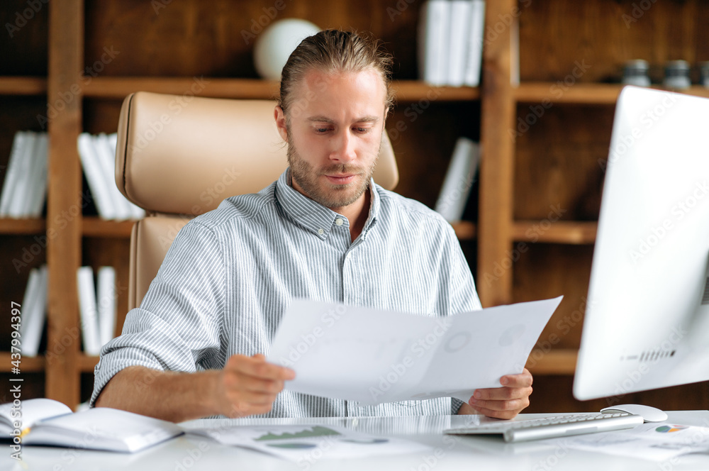 Serious focused smart caucasian manager, businessman or ceo, sitting in office at a table in formal attire, looking through business documents, thinking over financial strategy, analyzing profit Serious focused smart caucasian manager, businessman or ceo, sitting in office at a table in formal attire, looking through business documents, thinking over financial strategy, analyzing profit