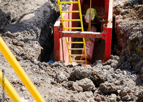 groundworker installing clay drainage pipe while in the trench supported by trench box photo