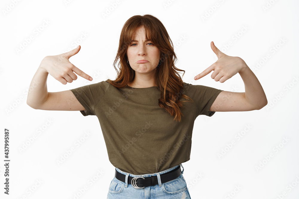 Disappointed girl complains and points fingers at logo, showing bad advertisement, being angry or offended, sulking displeased, standing against white background Disappointed girl complains and points fingers at logo, showing bad advertisement, being angry or offended, sulking displeased, standing against white background