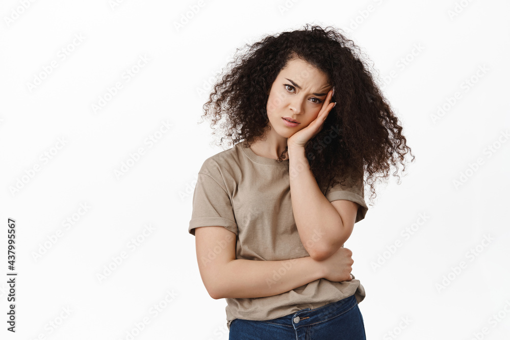 Sulking young woman lean on hand and looking with angry annoyed face at camera, pouting feeling upset, standing bored against white background