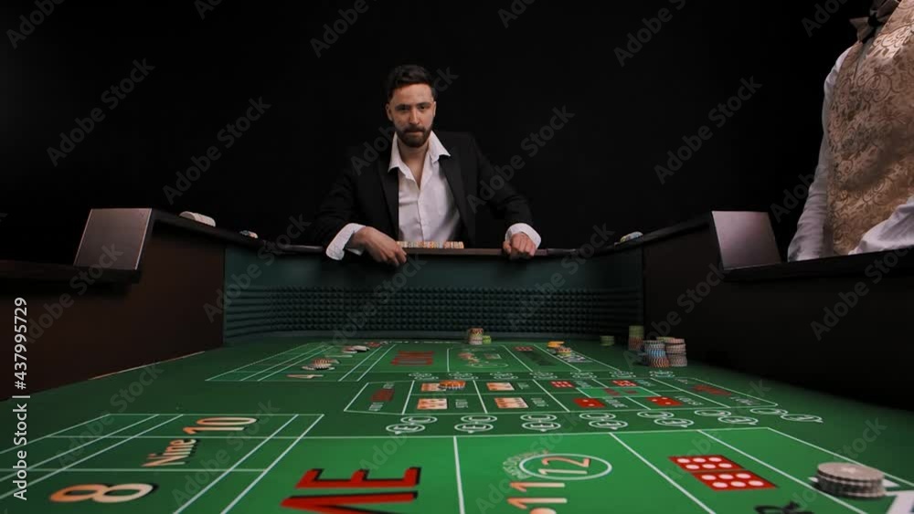 Men in business suit stand at a green craps table in a casino. The player rolls the dice and loses. The male are very upset and disappointed. View from inside of game table. Slow motion.