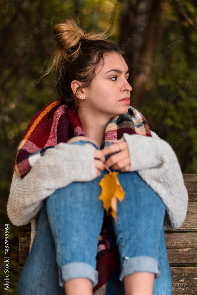 Portrait of a young teenage girl sitting on park bench with autumn leaf deep in thought Portrait of a young teenage girl sitting on park bench with autumn leaf deep in thought