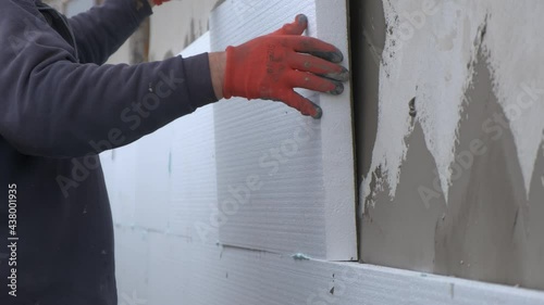 Construction worker installing styrofoam insulation sheets on house facade wall for thermal protection. photo