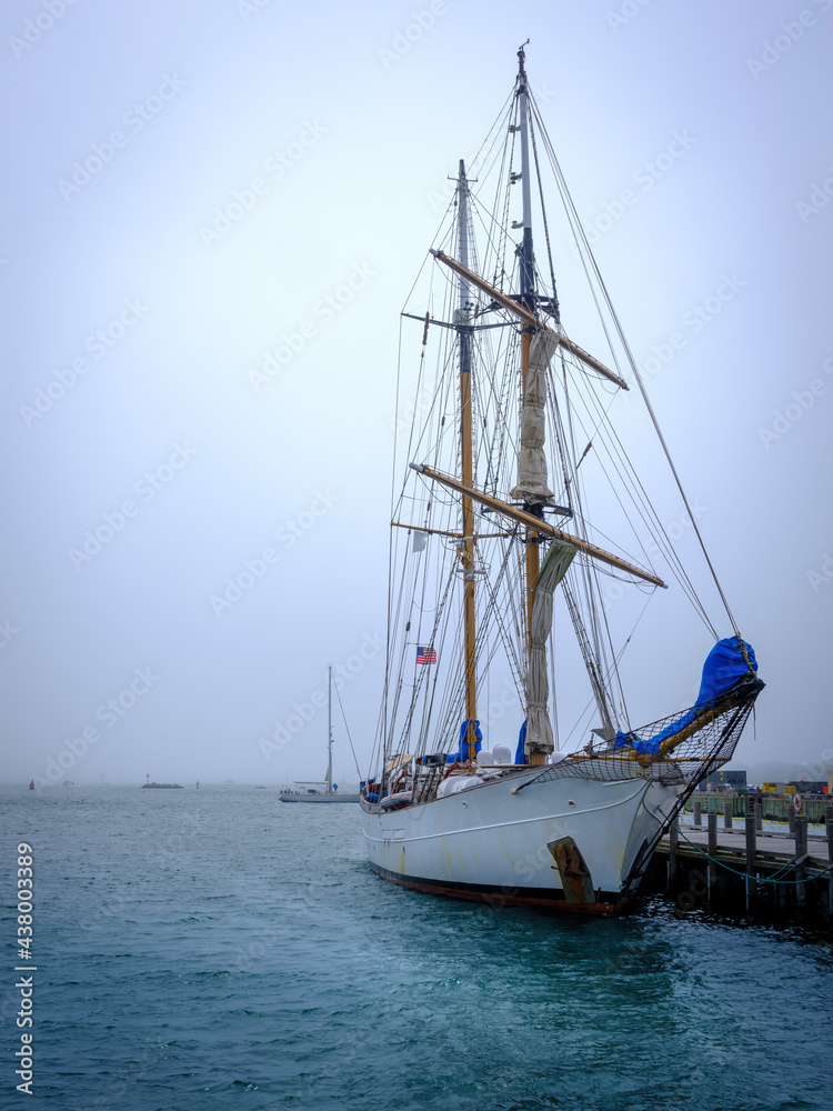 Sailboat moored at a commercial dock on a foggy morning. Seascape with white yacht over turquoise-colored seawater.