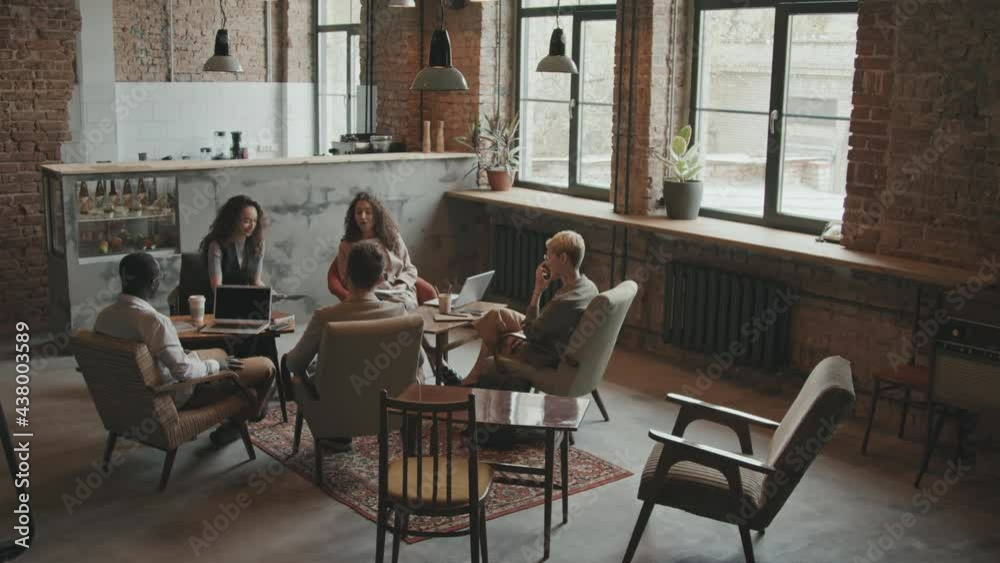 Full-shot slowmo of five multi-ethnic business men and women sitting in circle in modern coworking loft office and discussing business ideas Full-shot slowmo of five multi-ethnic business men and women sitting in circle in modern coworking loft office and discussing business ideas