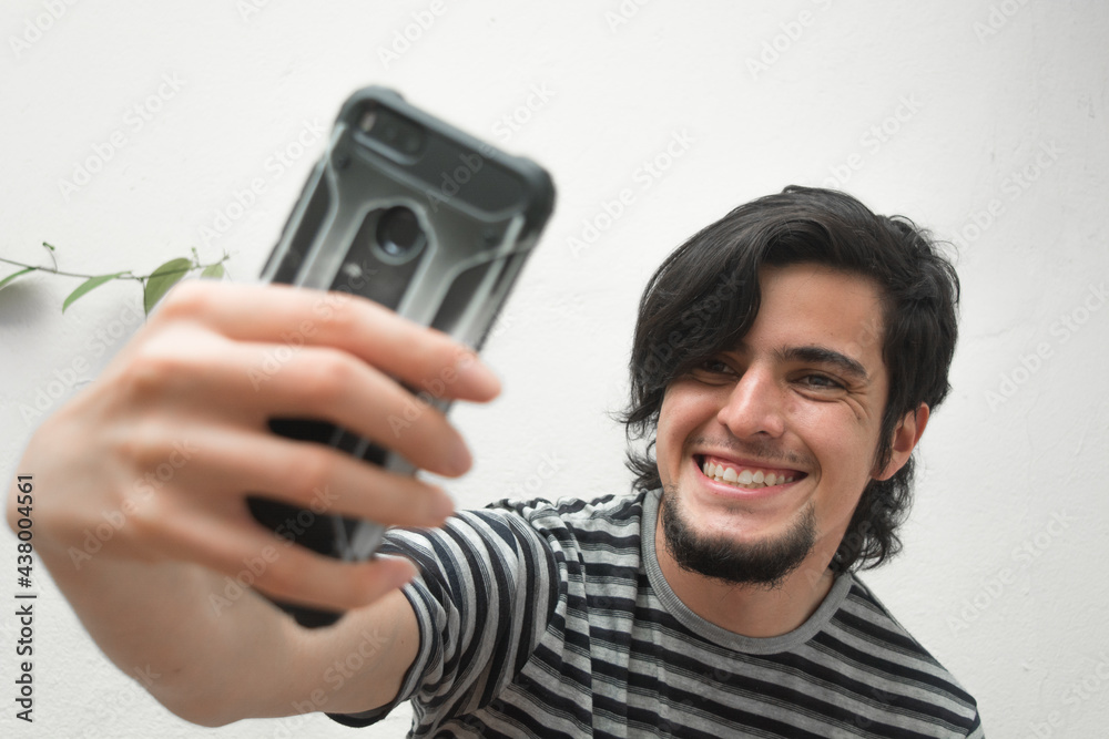 Portrait of a young man with beard holding a phone on his hand smiling and taking a selfie. Model wearing a black and white striped t-shirt. Happiness and confidence face or facial expressions. Portrait of a young man with beard holding a phone on his hand smiling and taking a selfie. Model wearing a black and white striped t-shirt. Happiness and confidence face or facial expressions.