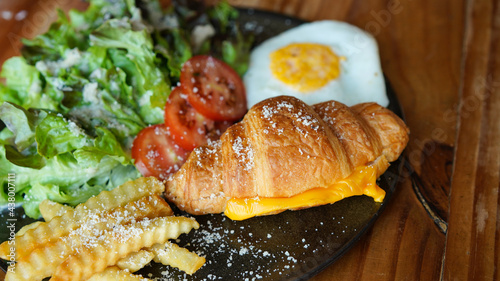 Vegetarian croissant with cheese and porched egg with french fries and vegetable. Healthy European breakfast