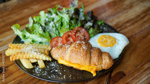 Vegetarian croissant with cheese and porched egg with french fries and vegetable. Healthy European breakfast