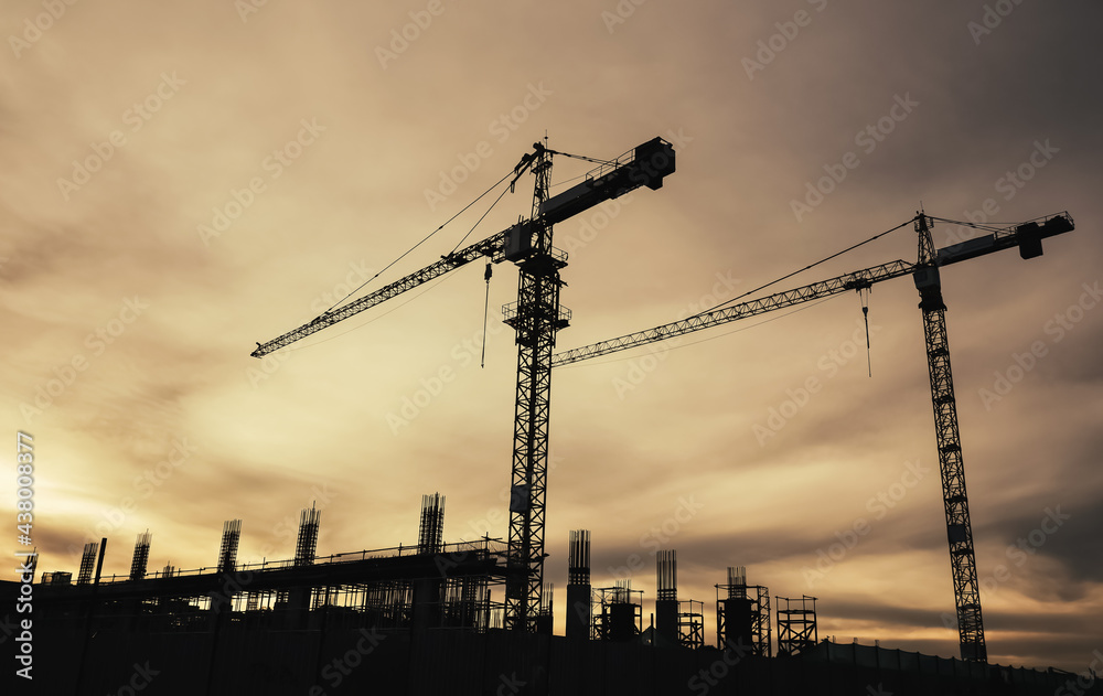 Silhouette of cranes in the construction site on the sunrise background. Residential building. Housing and condominium project. Industrial estate. Business Property development.