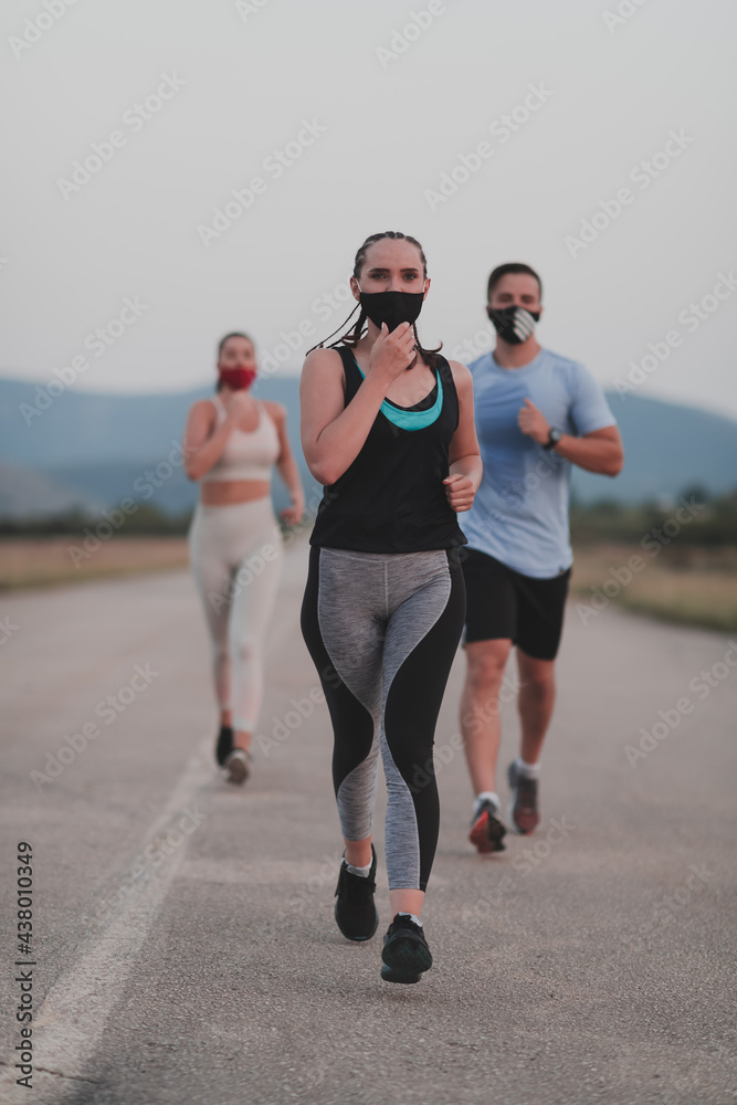 Multiethnic runners group wear face masks running keep social distance outdoor. Fit healthy diverse team wears sportswear jogging in evening on nature sports track distancing for safety. Multiethnic runners group wear face masks running keep social distance outdoor. Fit healthy diverse team wears sportswear jogging in evening on nature sports track distancing for safety.