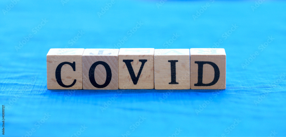 Fototapeta premium Covid virus word on wooden block on blue cloth with green light bokeh background as new normal because of COVID-19 virus., Corona virusl