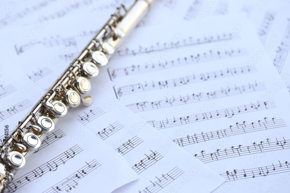 Flute, woodwind brass instrument in classical orchestra. Silver modern flute on white sheet music note for education and performance. Song composer on score sheet with green bokeh nature. Flute, woodwind brass instrument in classical orchestra. Silver modern flute on white sheet music note for education and performance. Song composer on score sheet with green bokeh nature.