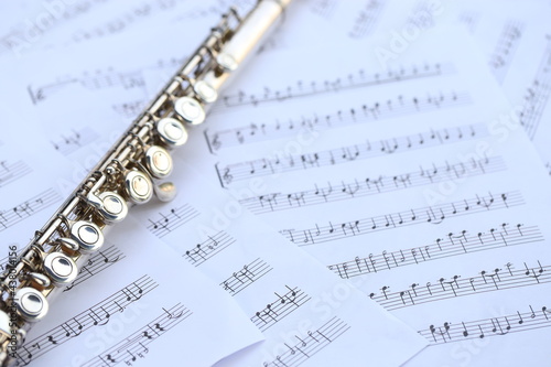 Flute, woodwind brass instrument in classical orchestra. Silver modern flute on white sheet music note for education and performance. Song composer on score sheet with green bokeh nature.