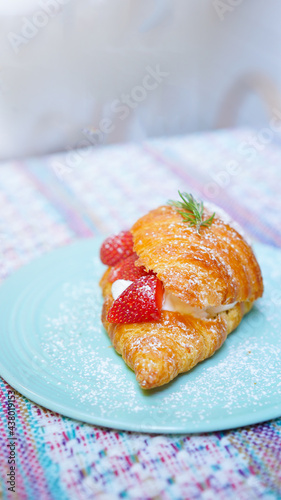 Croissant with strawberry and white softly mousse cream on blue ceramic plate with icing. French dessert assorted red berry.