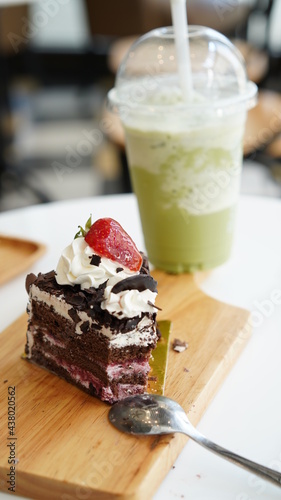 Chocolate cake sliced on wood plate with cold green tea milk in plastic cup in coffee shop.