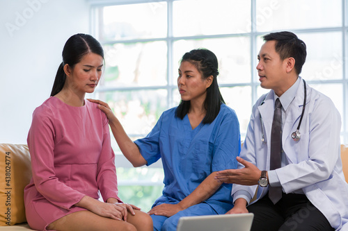 Doctor and nurse discussing treatment with woman patient and comforting at hospital. Group of doctor visiting and talking with Asian woman patient