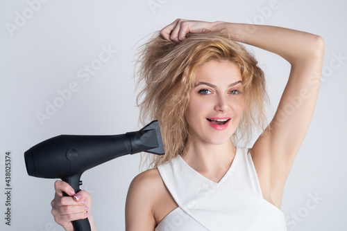 Health hair and beauty concept. Girl with blonde hair using hairdryer. Young attractive happy laughing blonde woman with hair dryer. Hairstyle, hairdressing concept.