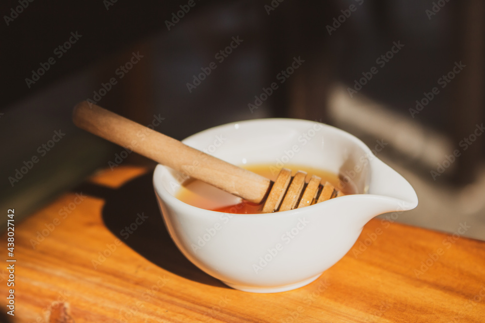 Honey with dipper in small white bowl. Homemade honey with wooden stick in sunlight. Honey in jar. Natural sweetener. Healthy nutrition. Natural dessert concept. Sweet food. Honey with dipper in small white bowl. Homemade honey with wooden stick in sunlight. Honey in jar. Natural sweetener. Healthy nutrition. Natural dessert concept. Sweet food.