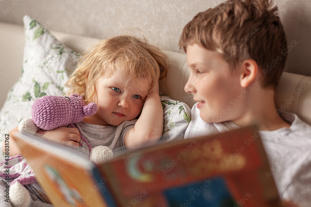 Obraz premium Cute happy favorite kids brother and sister reading book, on bed, getting ready bed. concept childhood, family