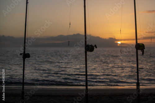 Colorful sunset with fishing rod on ocean. Silhouette of people and fishing rods.