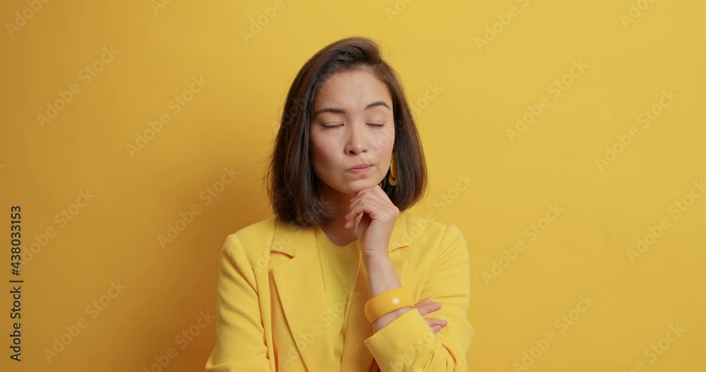 Pensive Asian lady ponders on something has pensive expression looks left and right makes decision dressed in formal clothes isolated over yellow background. Businesswoman considers something Pensive Asian lady ponders on something has pensive expression looks left and right makes decision dressed in formal clothes isolated over yellow background. Businesswoman considers something