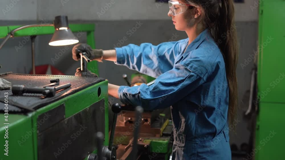 A female mechanic turner processes steel parts in a production workshop. The concept of an industrial worker in a factory.