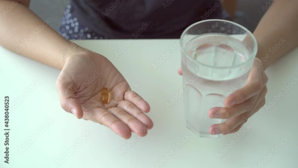 Asian woman holding a fish oil capsule on her hand and holding a drinking water Asian woman holding a fish oil capsule on her hand and holding a drinking water