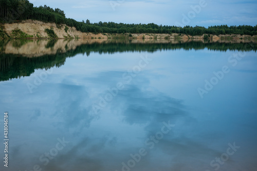 azure, water landscape against the blue sky. spruce forest, sandy cliff and clouds are reflected in the water surface.