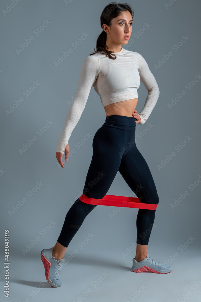 Woman performing legs workout with resistance band on grey background