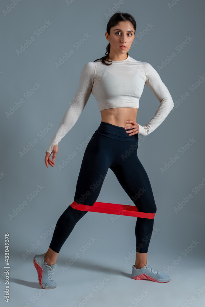Girl doing lower body exercises with resistance band on grey background