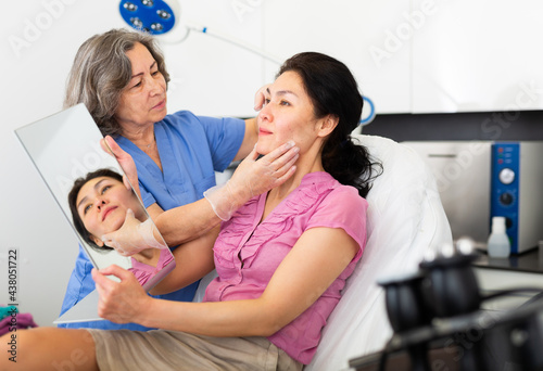 Skillful mature cosmetologist consulting woman in medical esthetic office