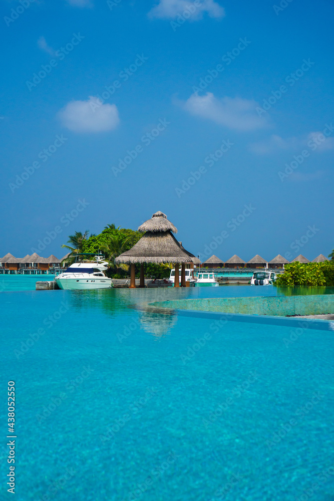 Scenic  landscape of Maldives beach and pier with speed boats and yachts on the horizon. Seascape with water bungalows, beautiful turquoise sea and lagoon waters, tropical nature paradise. 
