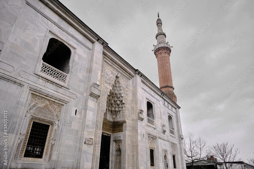 Fototapeta premium Bursa Turkey. Entrance gate of green mosque (Yesil camii) with magnificent carving and engraving works above the gate made of marble materials during rainy day with minaret made of bricks