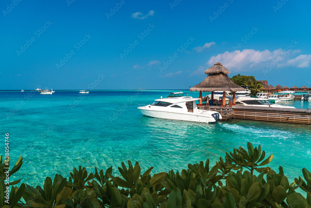 Fototapeta premium Scenic landscape of Maldives beach and pier with speed boats and yachts on the horizon. Seascape with water bungalows, beautiful turquoise sea and lagoon waters, tropical nature paradise. 