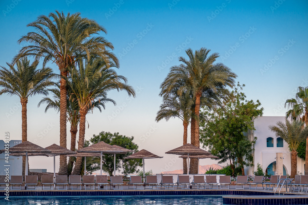 relaxing by the pool in a luxurious beachfront hotel resort at sunset enjoying perfect beach holiday vacation. Tropical swimming pool at sunrise. Summer holiday and vacation concept for tourism