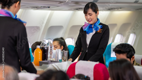 Two young beautiful Asian flight attendant serving food and drink to passengers on airplane. Two stewardess pushing food cart along aisle to serve the customer. Airline service business concept. photo
