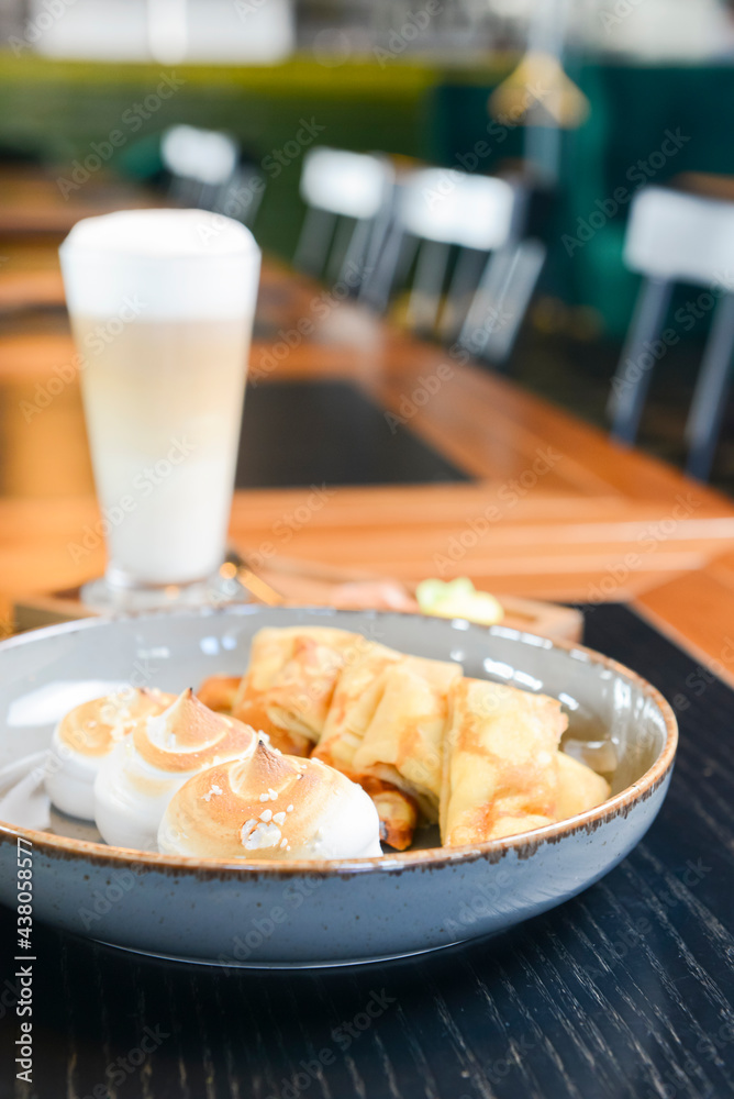 Close up of french style sweet crepes with soft cream served with a tall glass of coffee latte on a wooden table. Close up of french style sweet crepes with soft cream served with a tall glass of coffee latte on a wooden table.