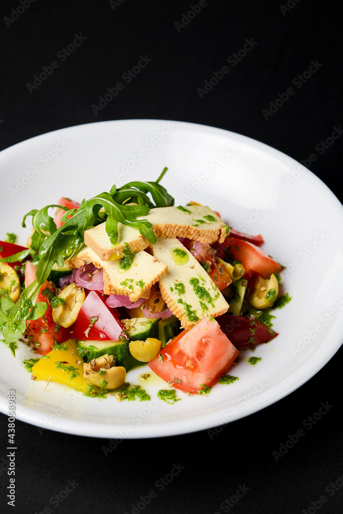 Vegetable salad with cheese, fresh romatoes and cucumbers, green olives served in a white plate over black background. Vegetable salad with cheese, fresh romatoes and cucumbers, green olives served in a white plate over black background.