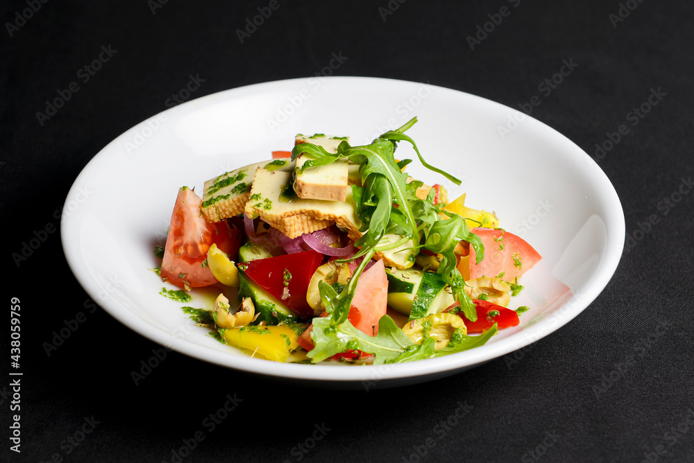 Vegetable salad with cheese, fresh romatoes and cucumbers, green olives served in a white plate over black background. Vegetable salad with cheese, fresh romatoes and cucumbers, green olives served in a white plate over black background.