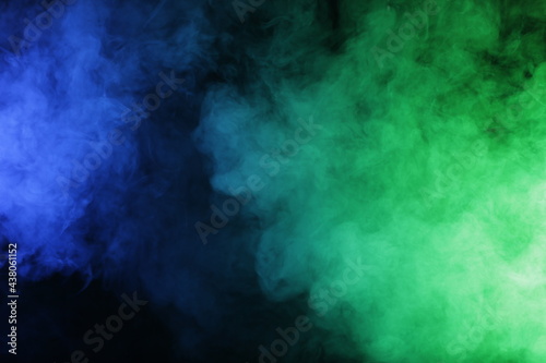 Artificial magic smoke in blue green light on black background
