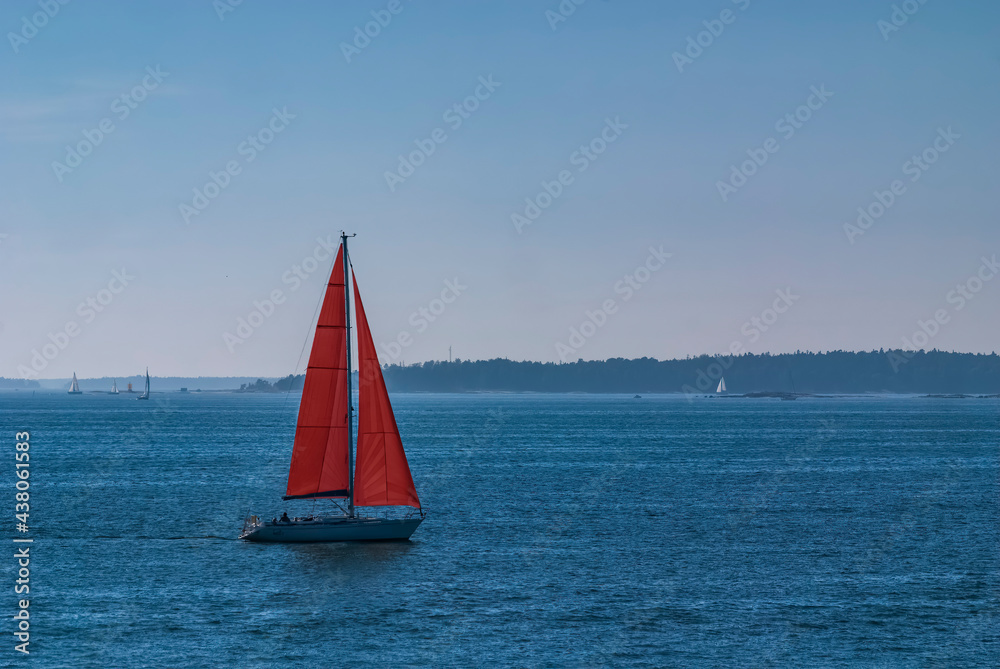 Red sailed sailboat in the Finnish gulf sea with other ships in background in mist 