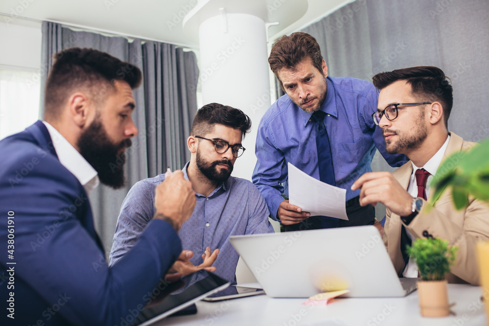 Male colleagues at meeting in office, sitting at table together, sharing ideas, discussing project strategy. Male colleagues at meeting in office, sitting at table together, sharing ideas, discussing project strategy.