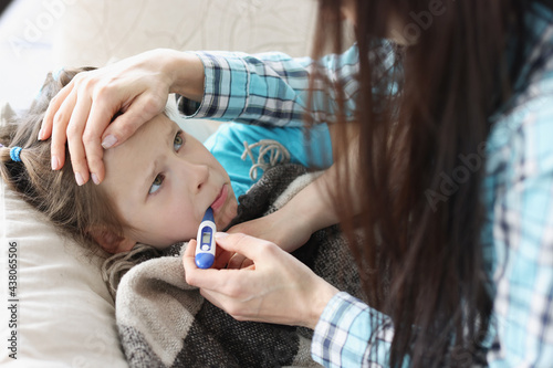 Mother measuring temperature of little girl with thermometer in her mouth