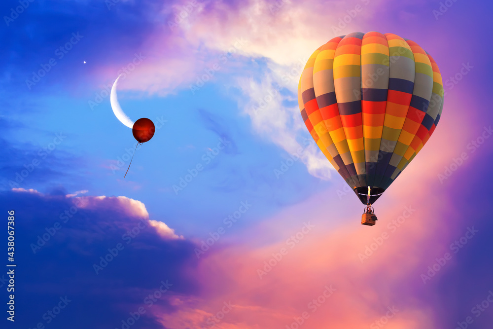 Obraz premium Hot air balloon flying in colorful evening sky with new moon shining. Only single red helium balloon flies up into the sky