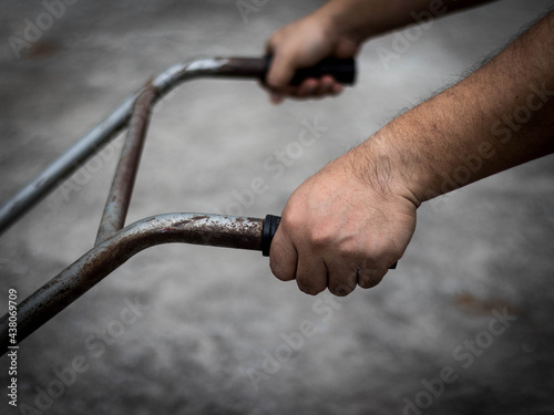 Hands held on the lever of an antique lawn mower, both hands are visible, the background is blurred, the edges are black.