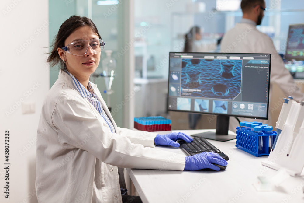 Portrait of scientist looking tired at camera sitting in modern equipped laboratory, typing on pc. Chemist examining virus evolution using high tech for scientific research, vaccine. Portrait of scientist looking tired at camera sitting in modern equipped laboratory, typing on pc. Chemist examining virus evolution using high tech for scientific research, vaccine.